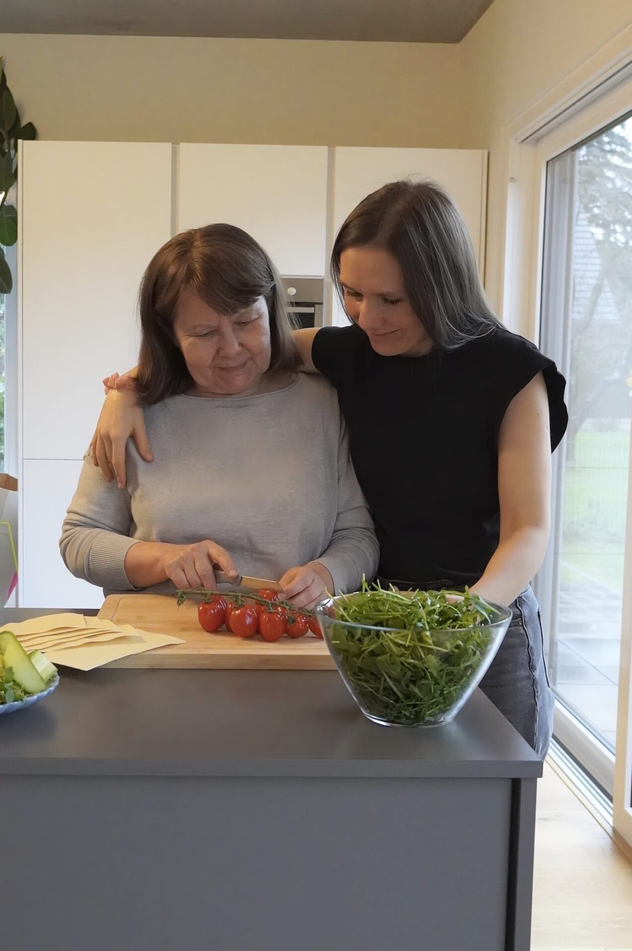 Mother and daughter are cooking in the kitchen. They are cutting tomatoes and making lasagna. 