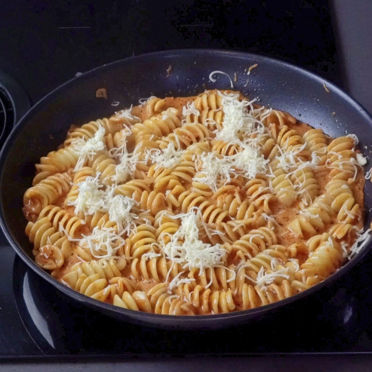 Adding grated cheese to the creamy pasta sauce in the pan.