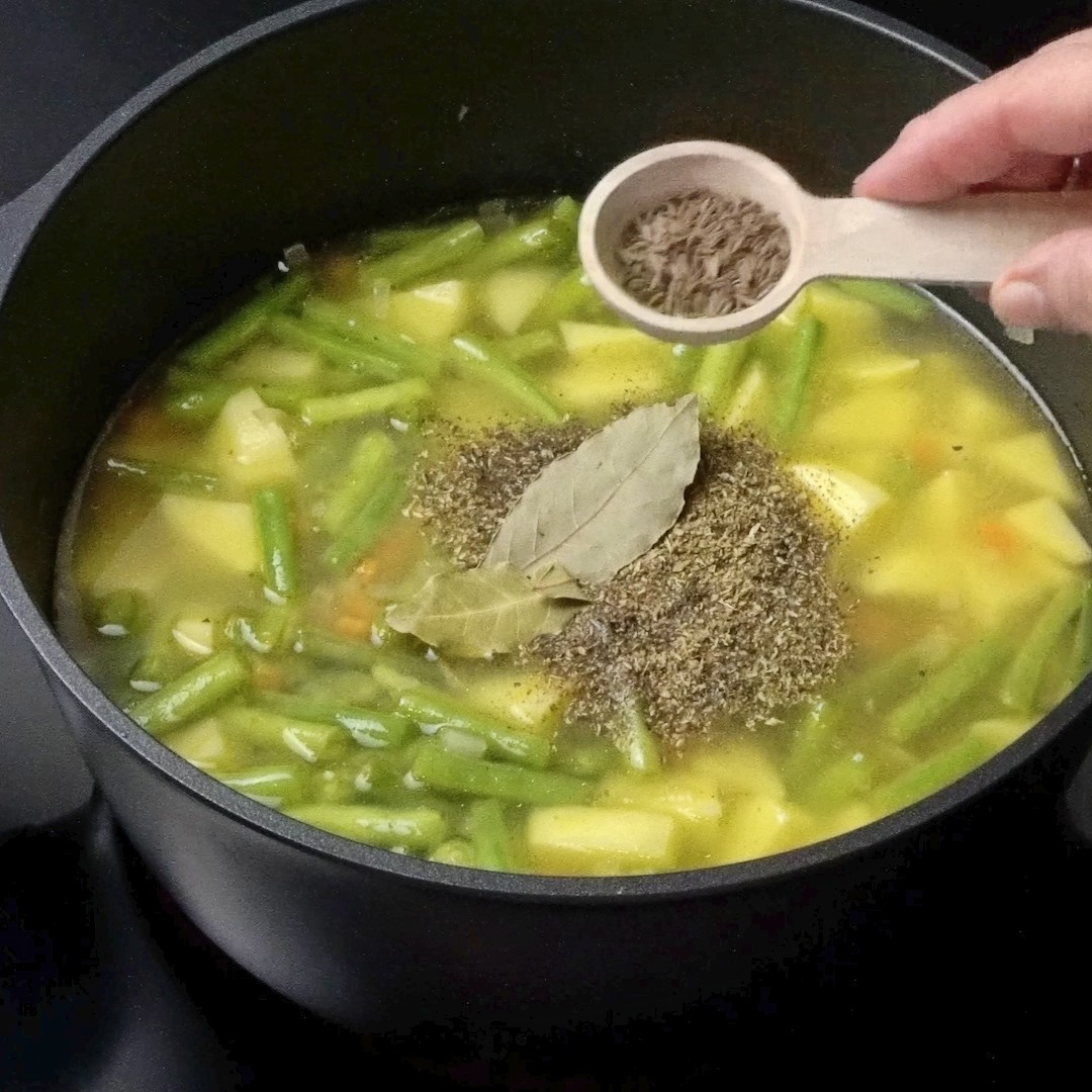 Adding cumin seeds to the pot for aromatic flavor.