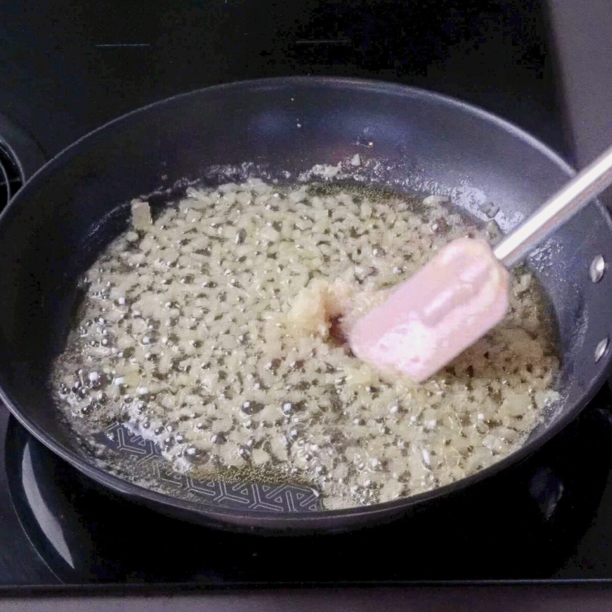 Stirring minced garlic in a hot pan with oil and onions.