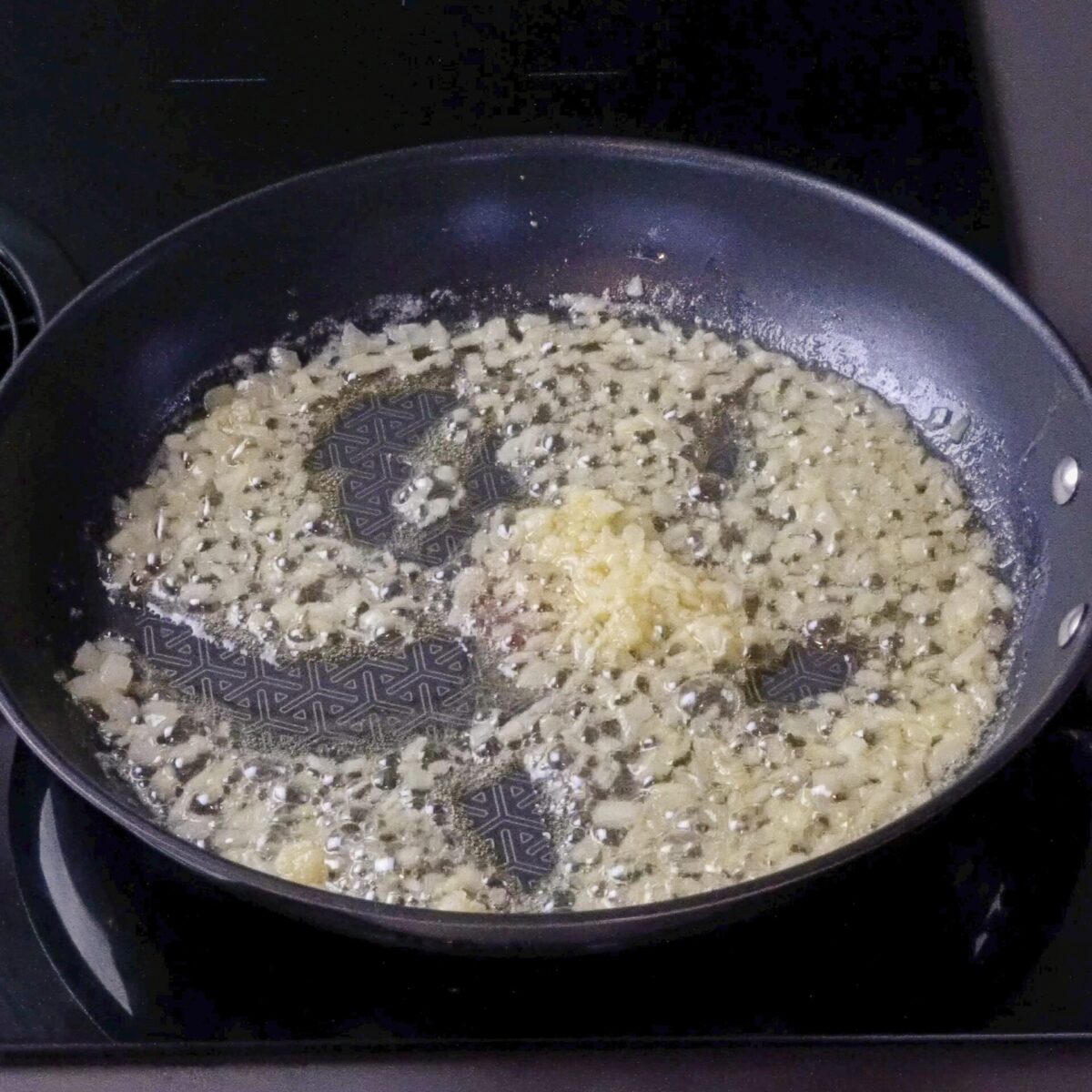 Adding minced garlic to the pan with sautéed onions.