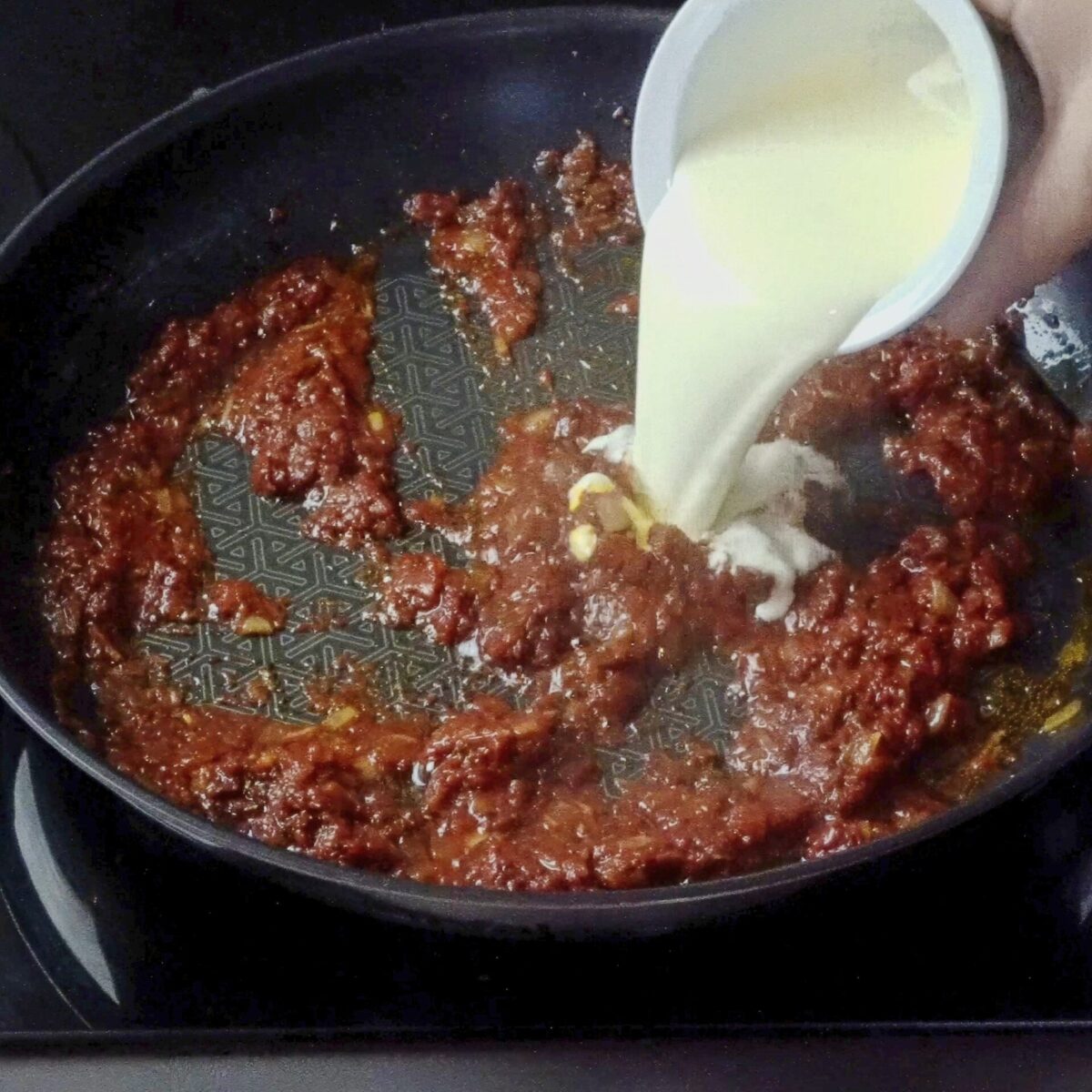 Pouring heavy cream into the sauce in the pan.