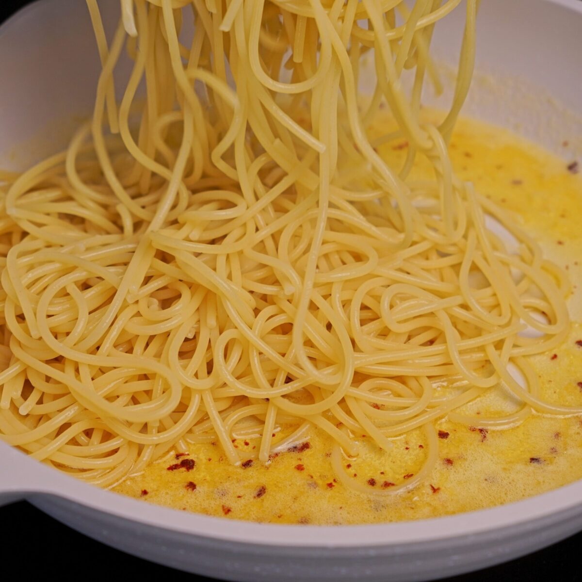 Adding cooked pasta to lemon butter sauce in a pan.