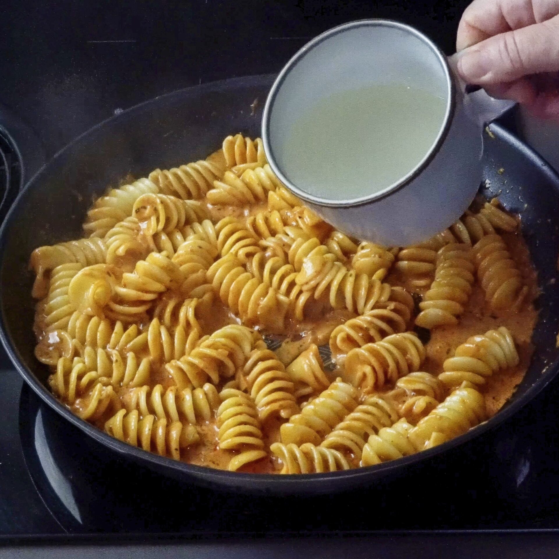 Adding more pasta water to the pan to loosen the sauce.