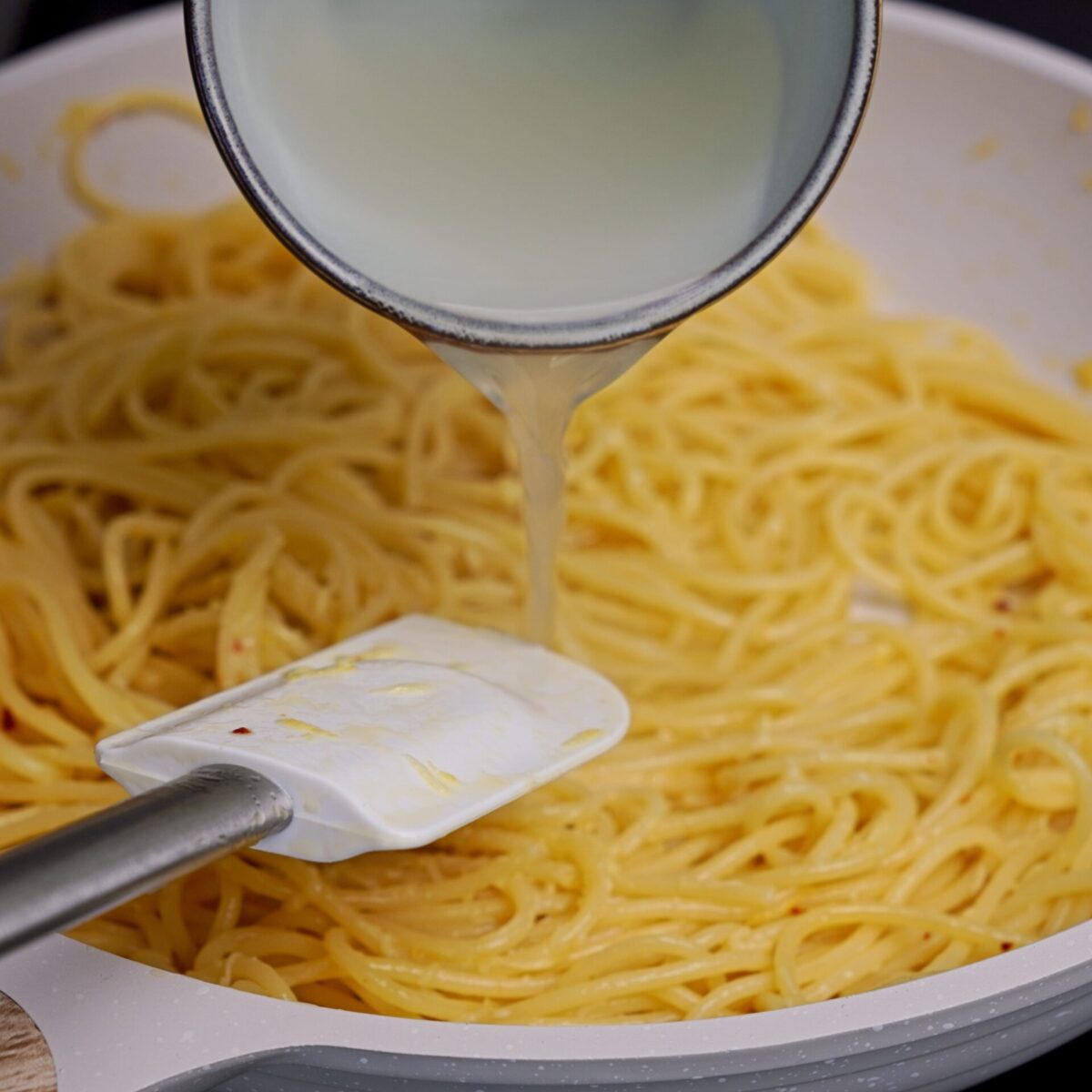 Pouring reserved pasta water into the pan with lemon butter pasta.