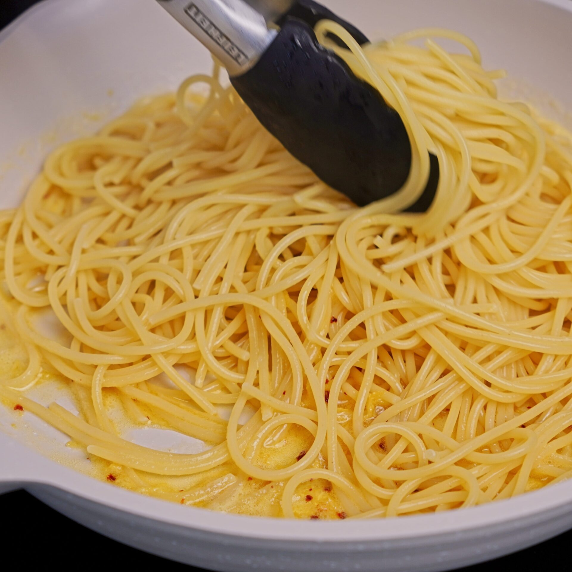 Mixing pasta with lemon butter sauce in a pan.