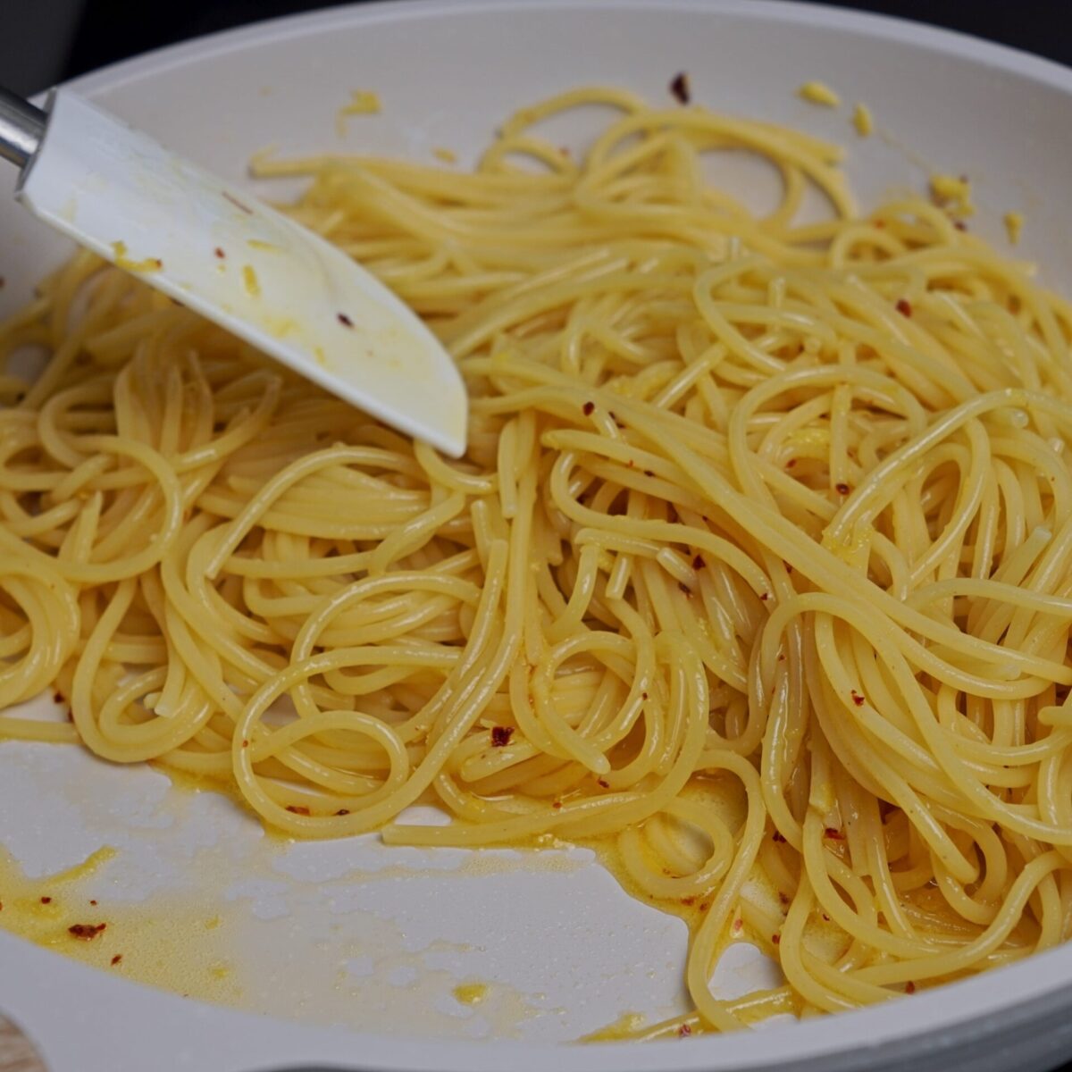 Combining pasta and sauce in a pan for an even coating.