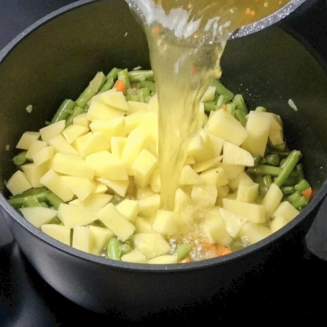 Adding stock to the pot with beans and potatoes.