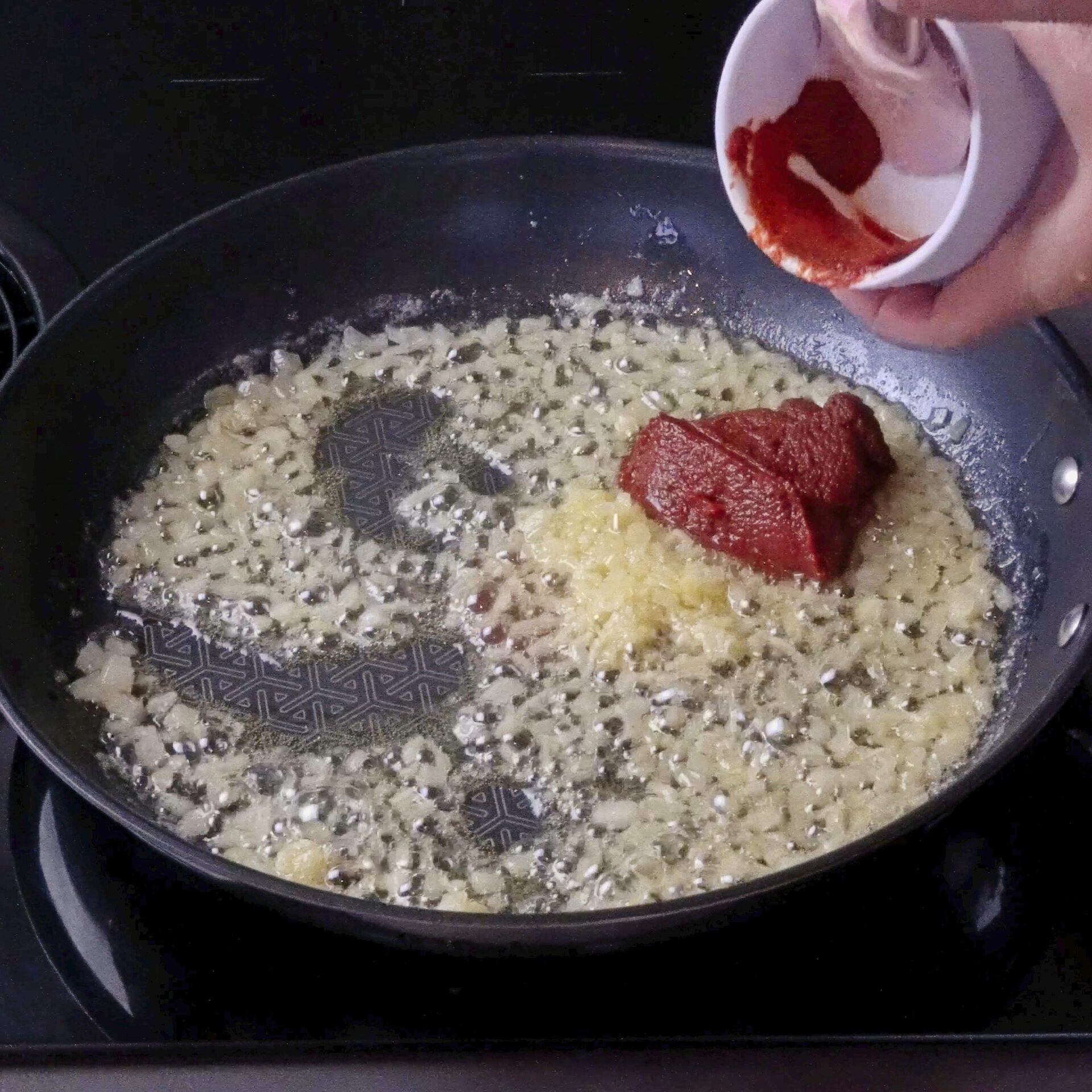 Adding tomato paste to the pan with sautéed garlic and onions.