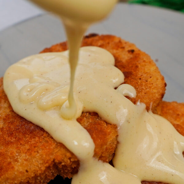 Pouring homemade Alfredo sauce over crispy vegetarian schnitzel.
