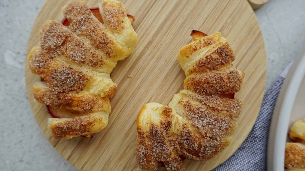 Two puff pastry croissants viewed from above. The tops are dusted with cinnamon sugar, giving them a cinnamon brown hue, while the sides remain untouched, displaying their golden pastry.