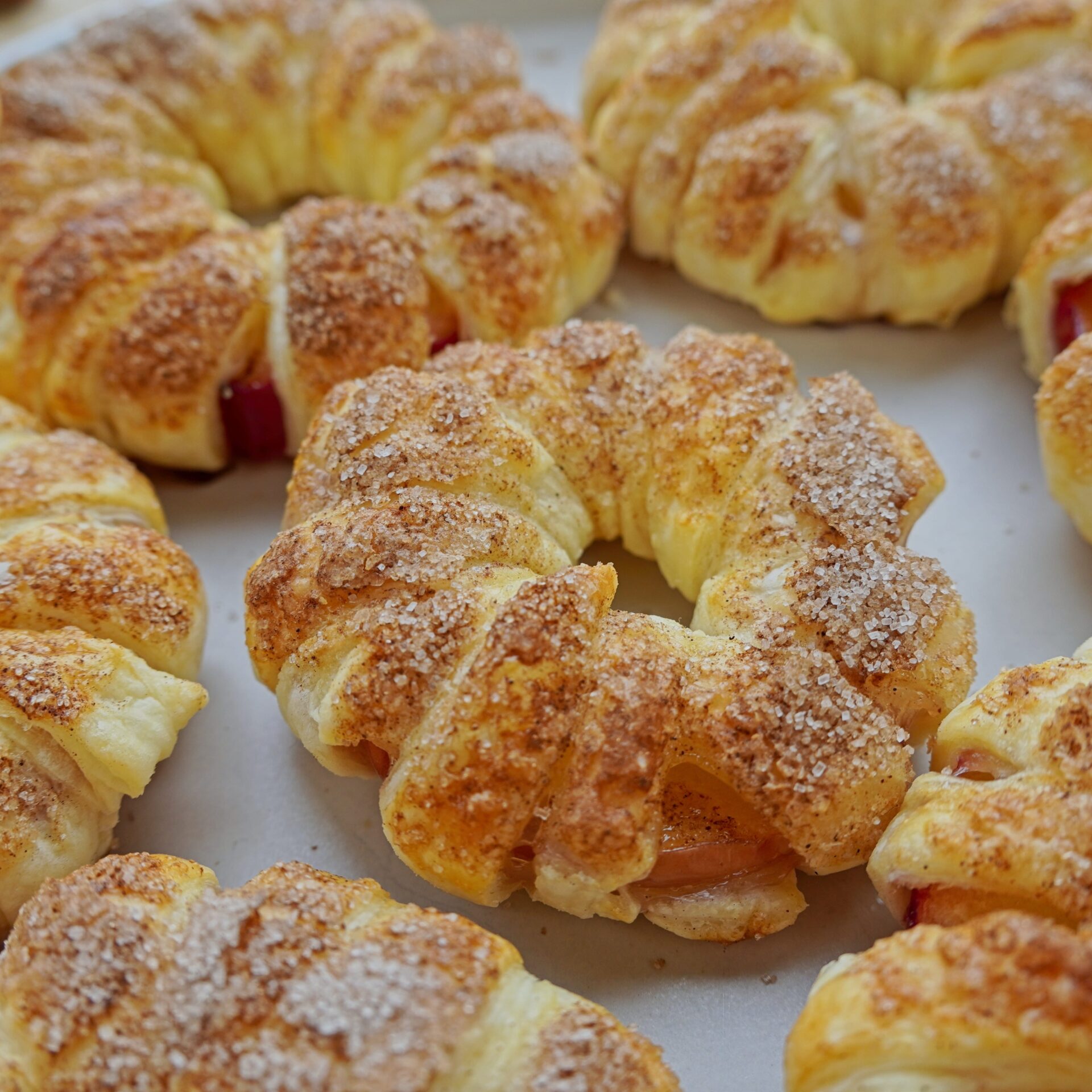 A close-up of apples in pastry, with puff pastry stripes around apples. The dessert is sprinkled with cinnamon sugar for extra crispiness.