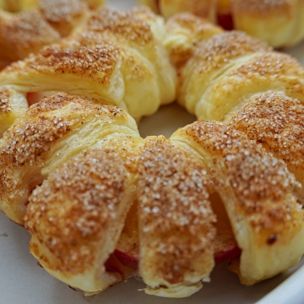 A close-up on one apple in puff pastry dessert. On puff pastry strings there are sugar grains and cinnamon grains on top.