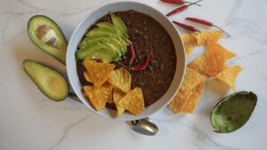 Black bean soup in a bowl with avocado and nachos on top.