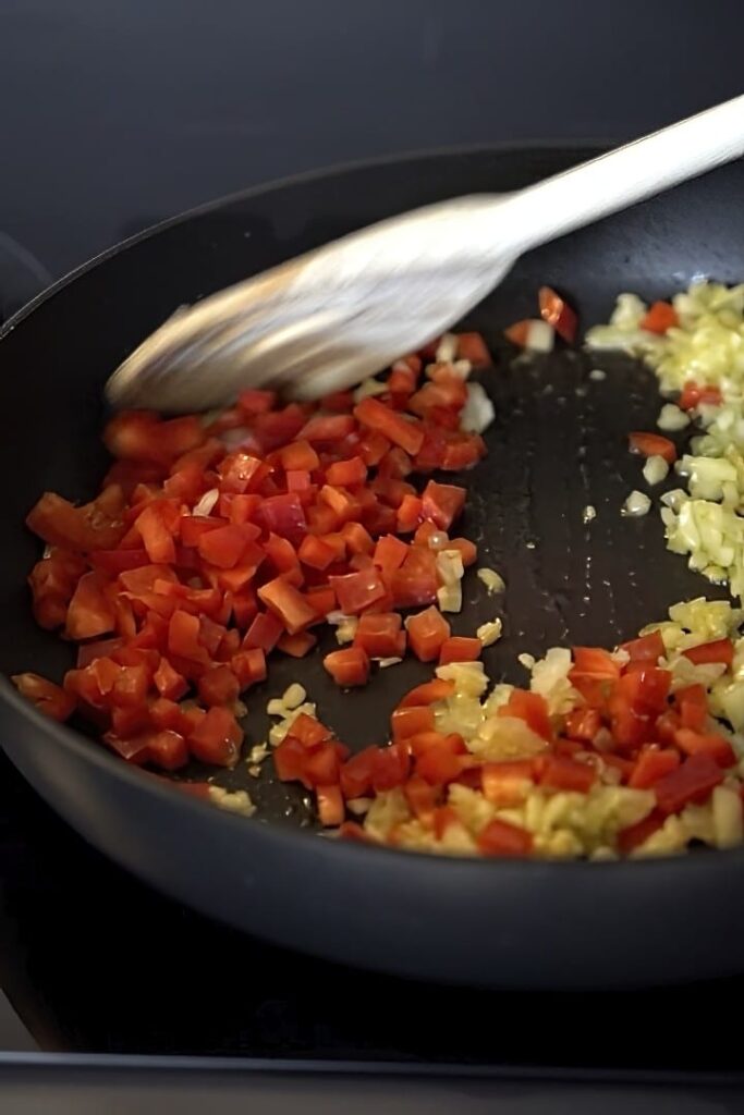 Adding bell pepper to a pan and mixing.