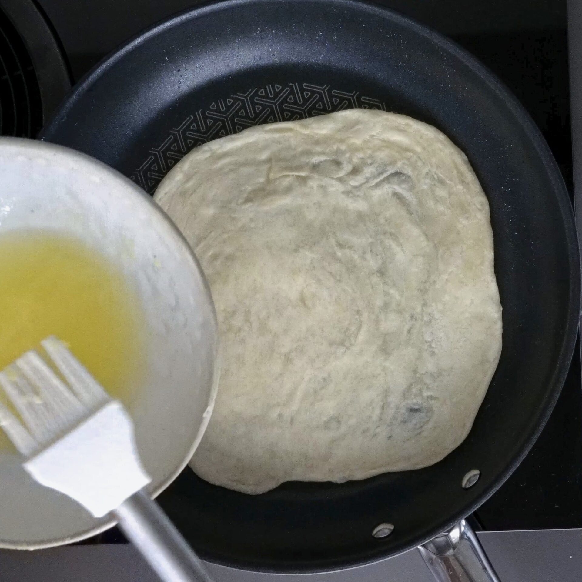 Brushing oil and butter on roti while cooking in the pan.