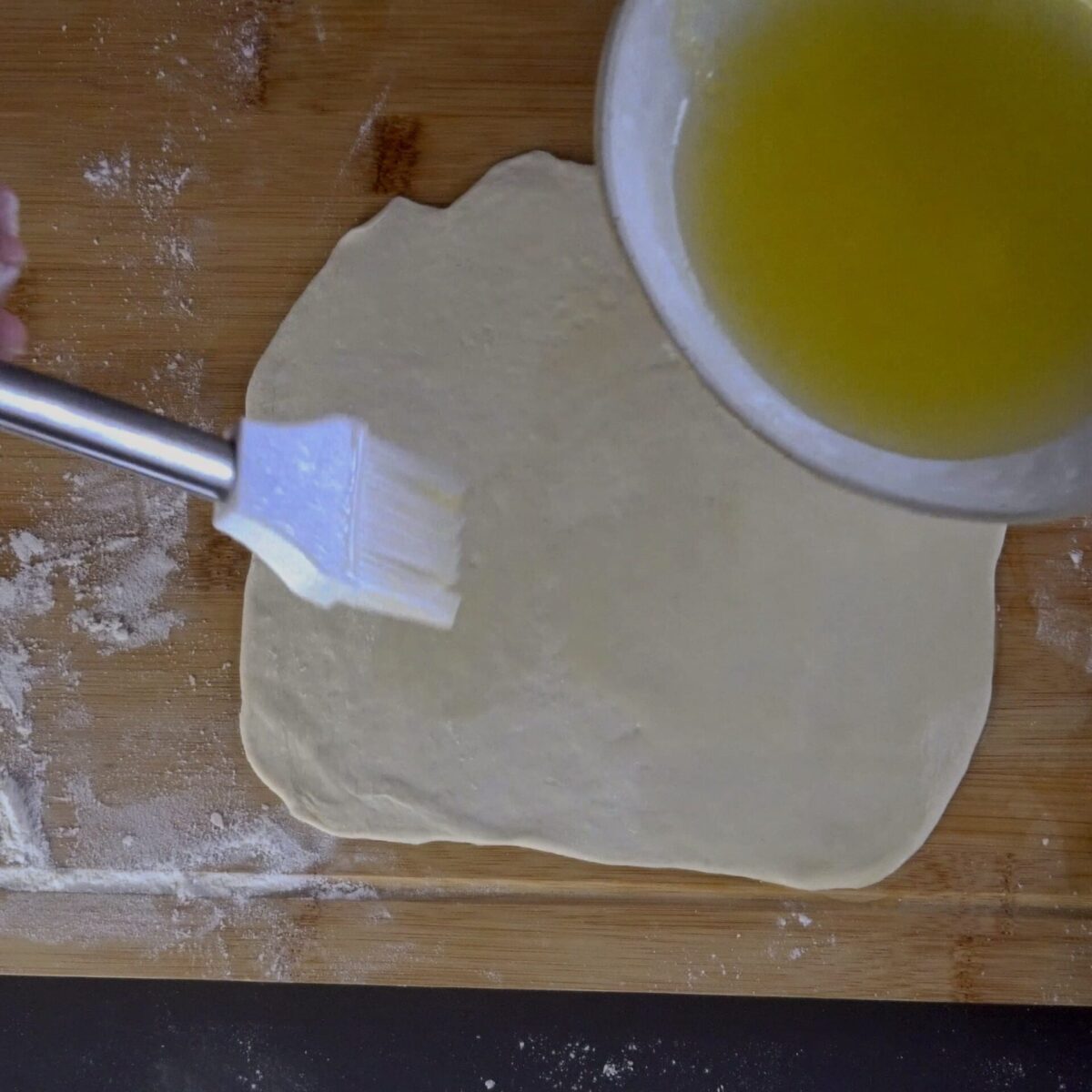 Brushing the dough with butter and oil to create flaky layers.