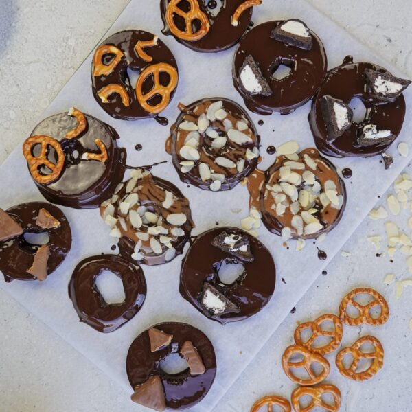 Chocolate-covered apple slices with various toppings on a cutting board, ready to chill in the fridge.