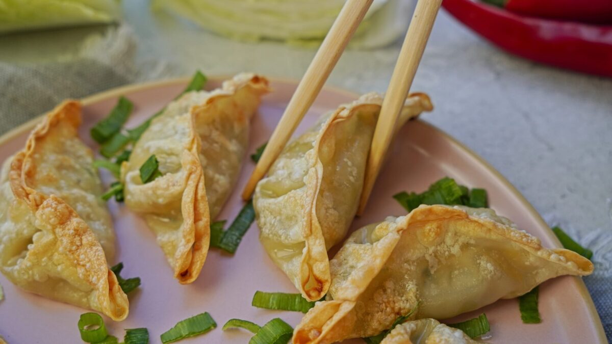 Person picking up a crispy gyoza from a plate with chopsticks.