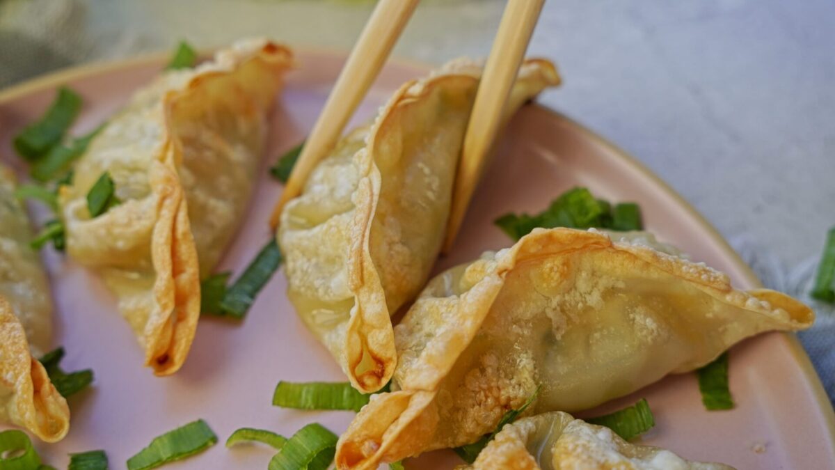 Holding a crispy air-fried frozen gyoza with chopsticks.