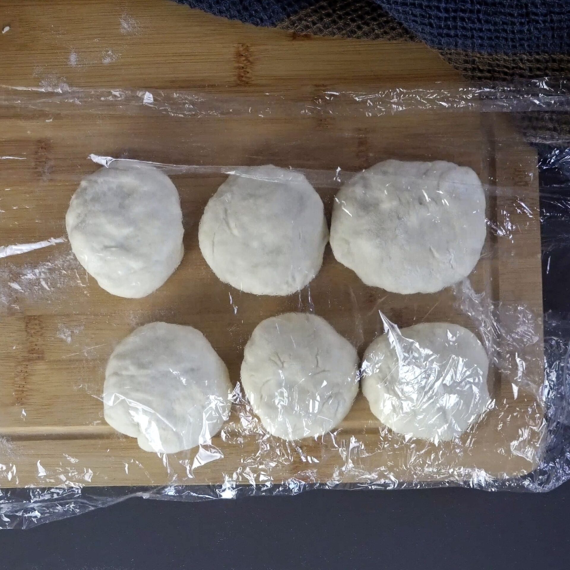 Covering dough balls with plastic wrap to rest and soften.