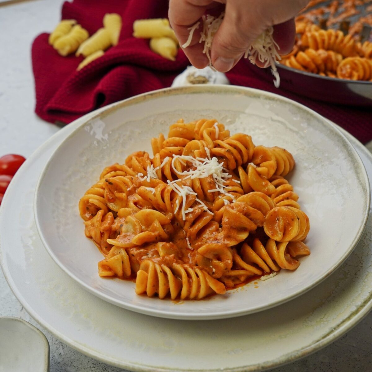 A person sprinkling grated cheese over pasta in creamy tomato sauce.