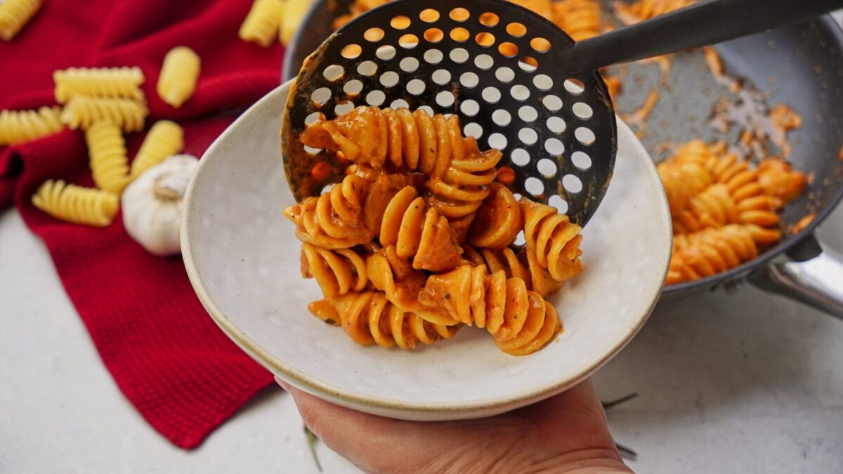 Ladling freshly cooked tomato cream pasta into a bowl.