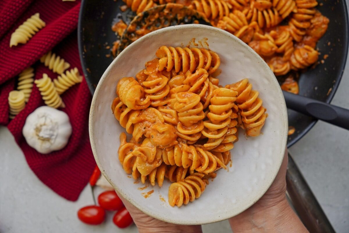 A person holding a bowl of warmed creamy tomato pasta.
