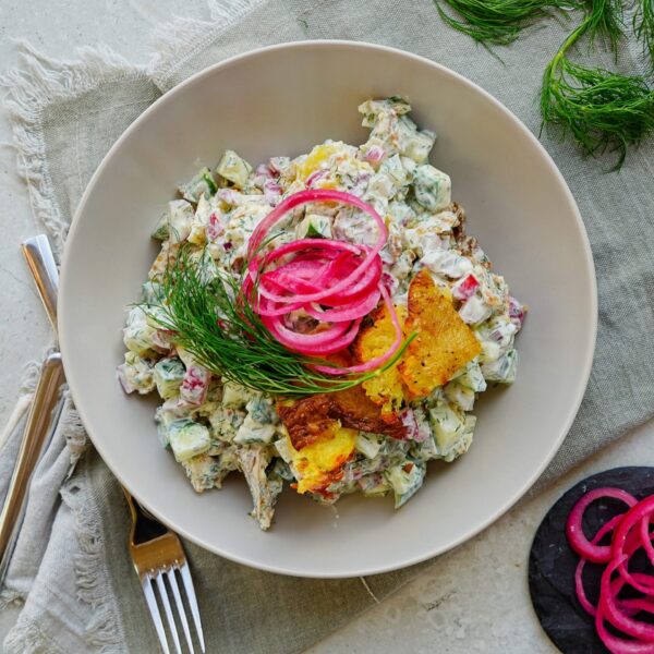 Crispy potato salad in a bowl decorated by crispy potatoes, red onions and dill.