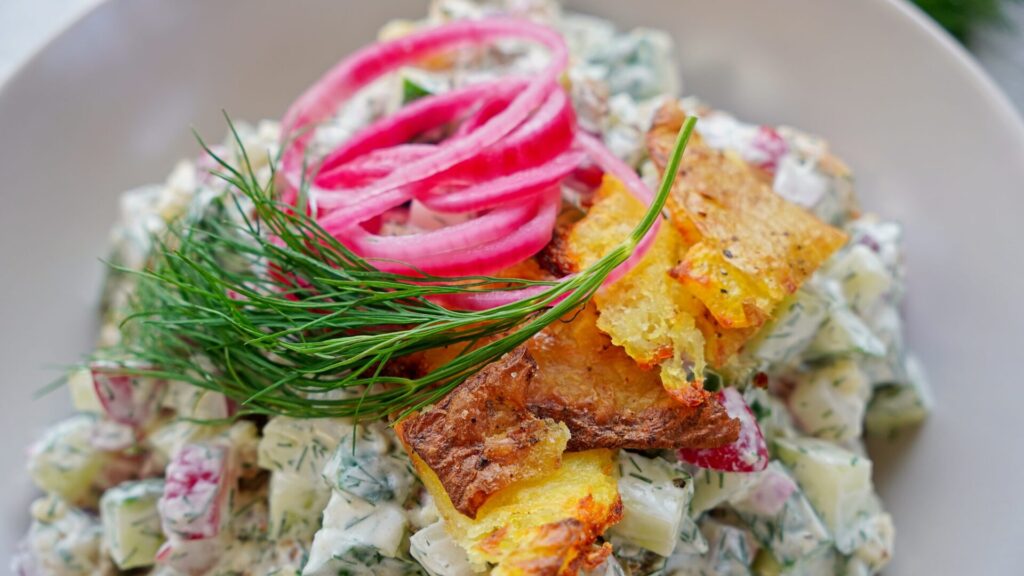A close up of crispy mashed potato salad with crispy potatoes, pickled red onions and dill on top. 