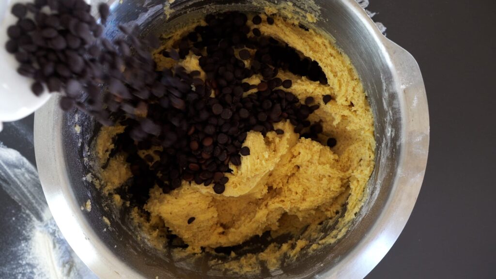 Adding chocolate chips to the cookie dough batter and mixing.