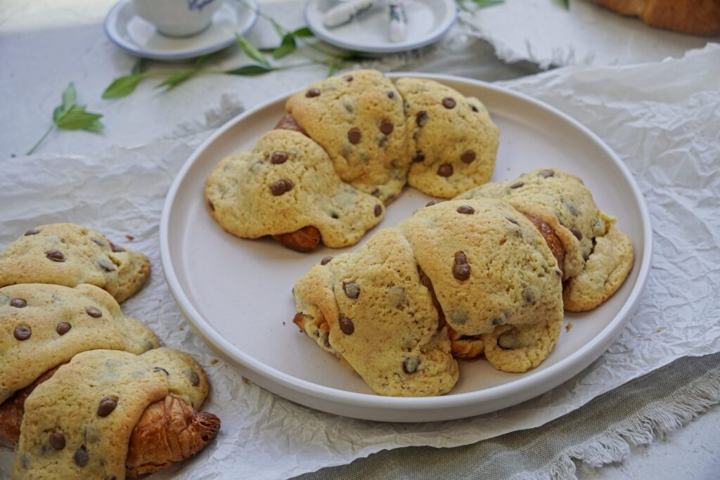 Close-up of three freshly baked croissant cookies on a decorated table with cups and plates, ready for coffee.