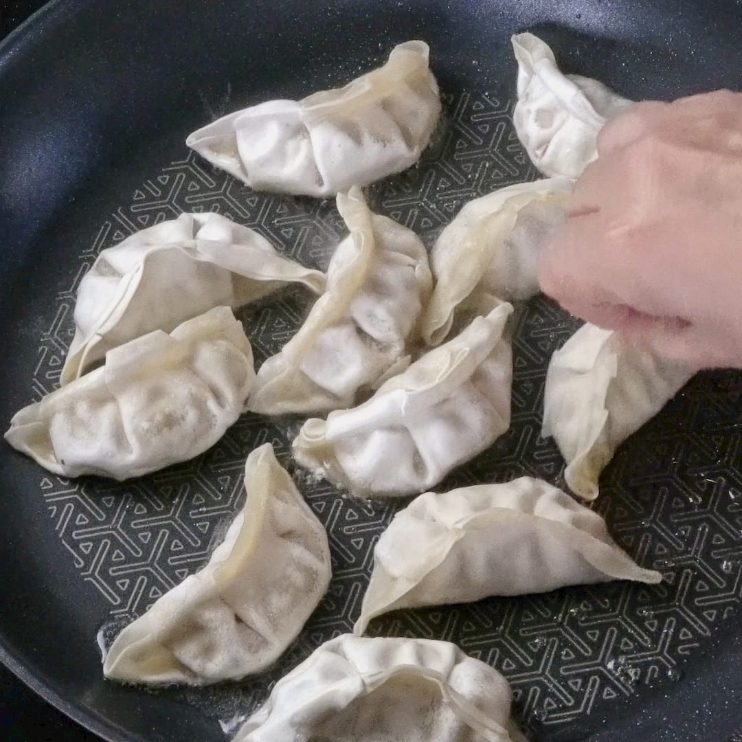 Dipping frozen dumplings before frying in a pan.