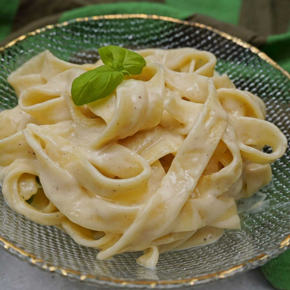 Easy fettuccine Alfredo pasta in a bowl with extra creamy sauce and basil leaves.