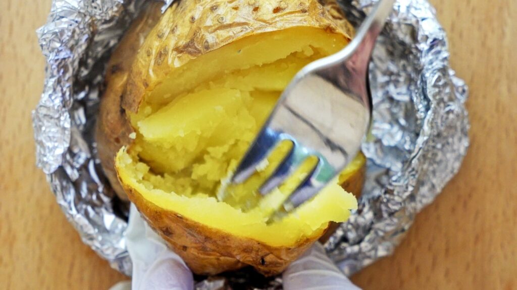 Mashing potatoes with a fork before adding cheese and butter.