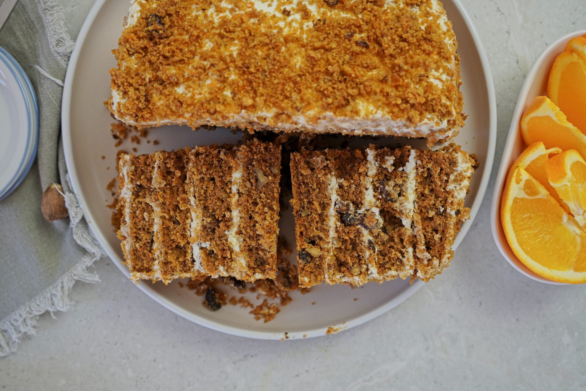 Freshly baked carrot cake, cut in half with cream cheese layers, ready to be wrapped in plastic wrap and stored in a container.