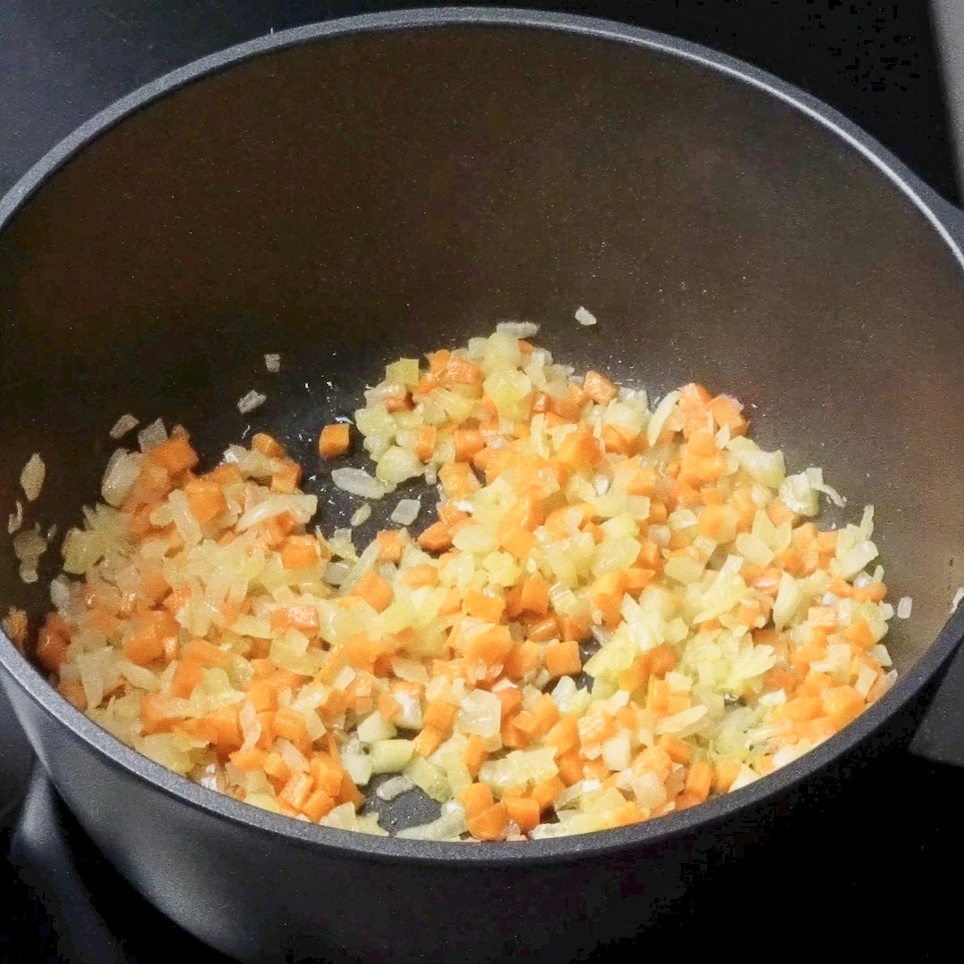 Sautéing carrots and celery in a pot until softened.