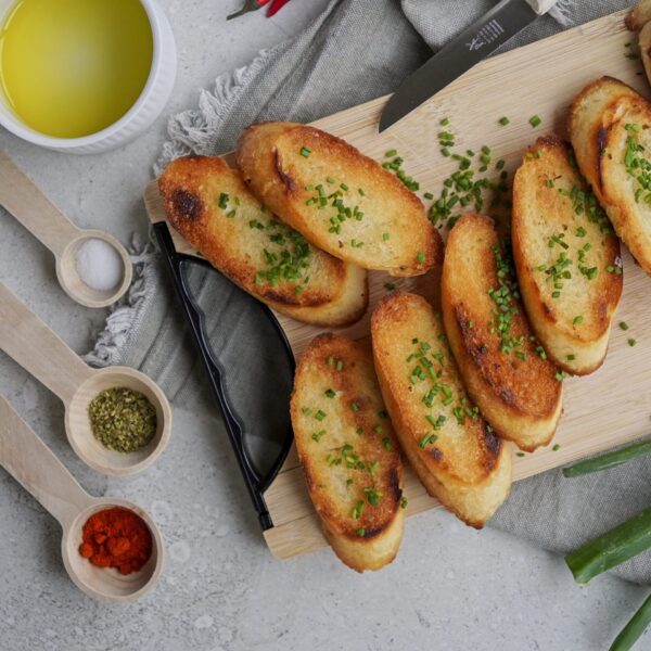 Garlic bread made with sliced bread on a cutting board, topped with fresh herbs and green onion.