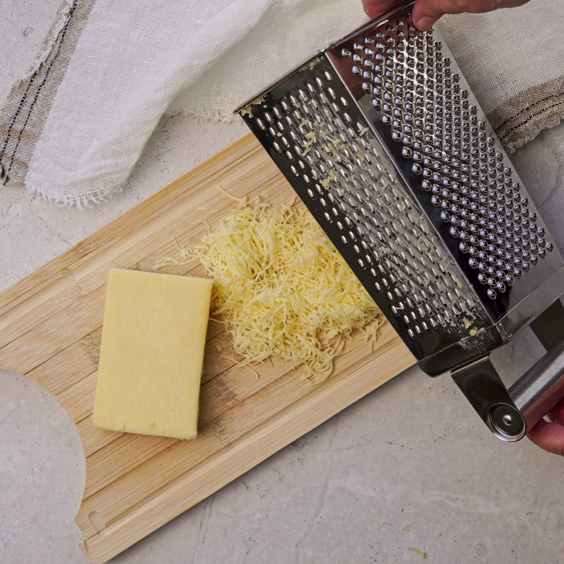 A block of cheese on a cutting board with grated cheese and a grater beside it.