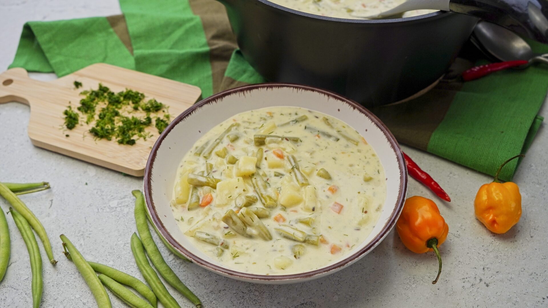 Delicious creamy green bean potato soup with fresh dill, with a pot in the background.