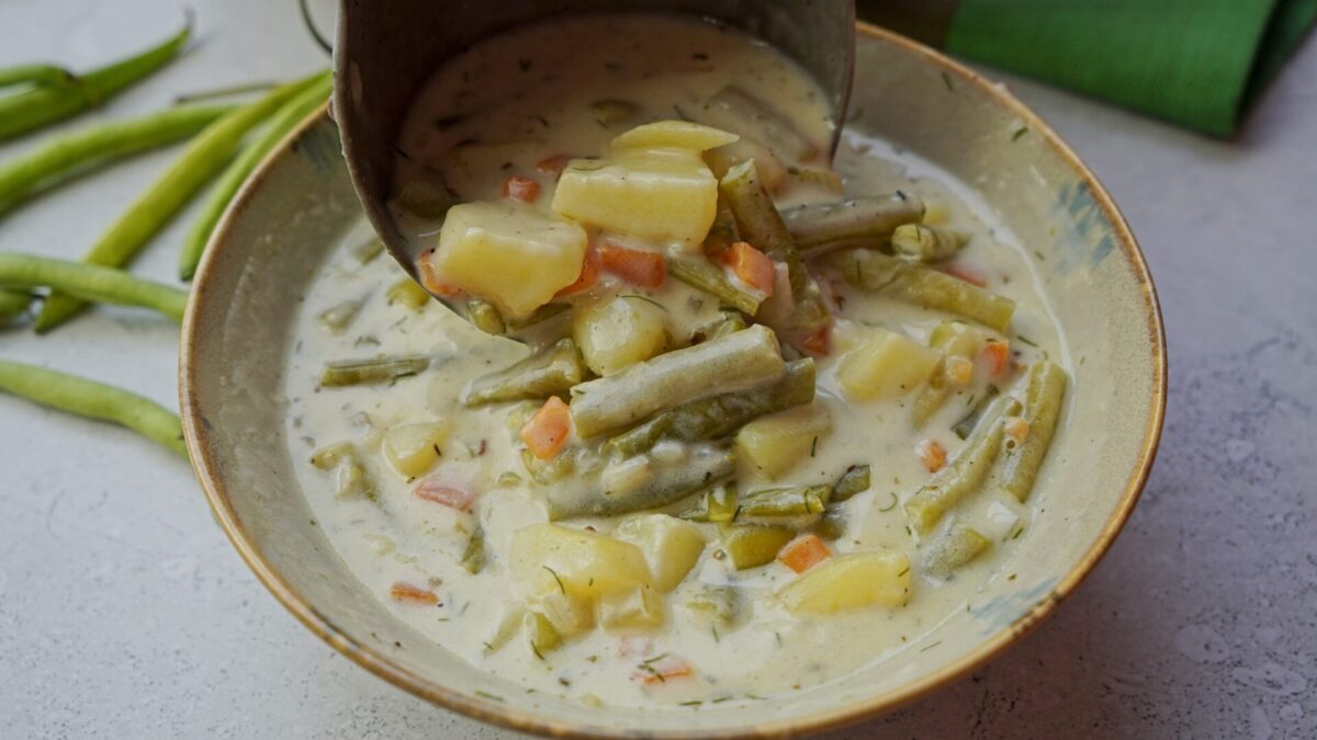 Pouring green bean soup from a ladle into a bowl.