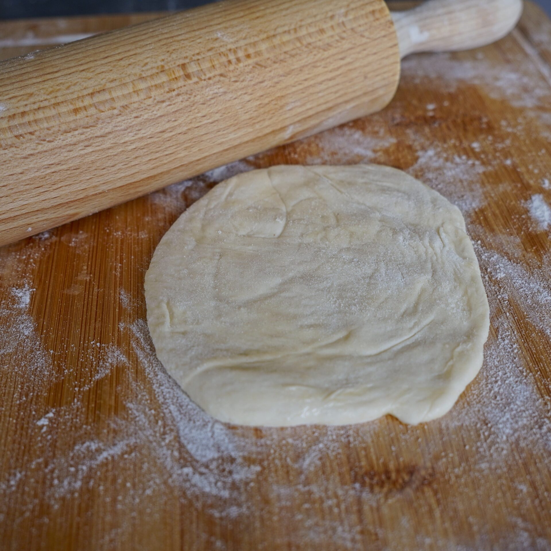 Dough with flour and a rolling pin on a wooden surface while making roti.
