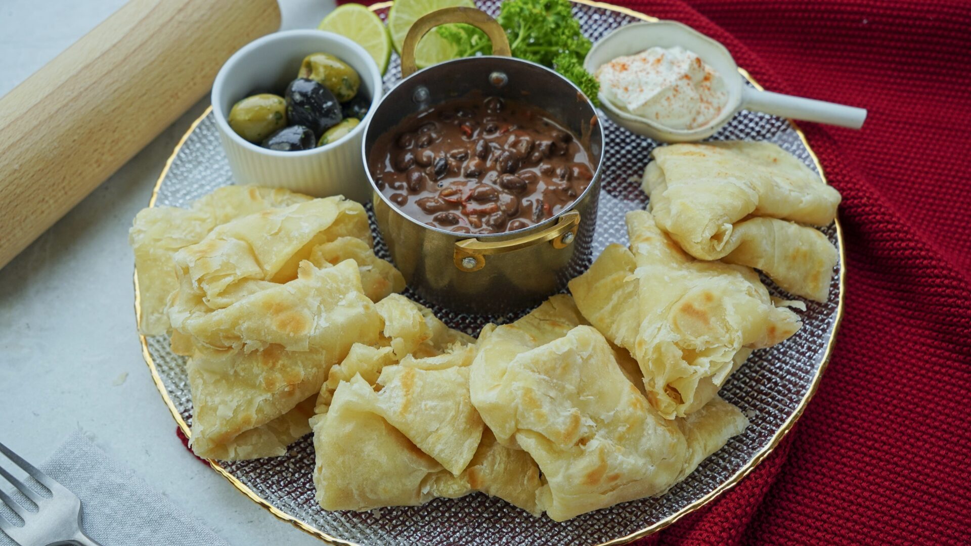 Oil roti with thin layers served alongside black bean soup, Greek yogurt, and olives.