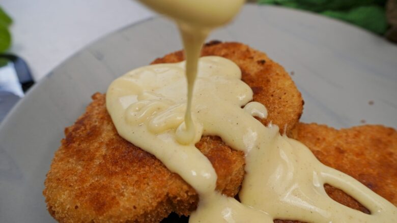 Pouring homemade Alfredo sauce over crispy vegetarian schnitzel.