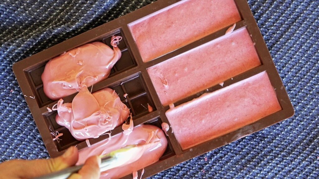 Pouring pink chocolate into a mold before refrigerating.