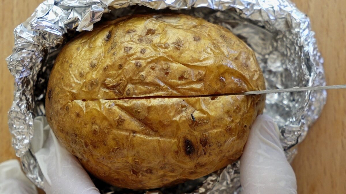 Cutting baked potatoes before adding butter and cheese.