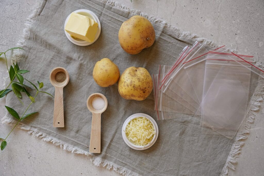 Ingredients and equipment for freezing baked potatoes: potatoes, butter, mozzarella cheese, salt, pepper, and Ziploc bags.