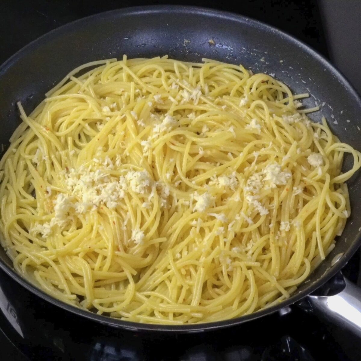 Adding grated cheese to pasta in lemon butter sauce.