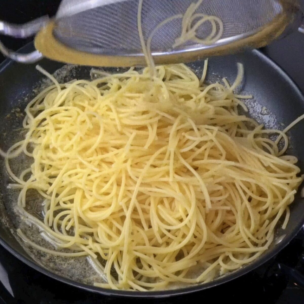 Adding cooked pasta to lemon butter sauce in a pan.