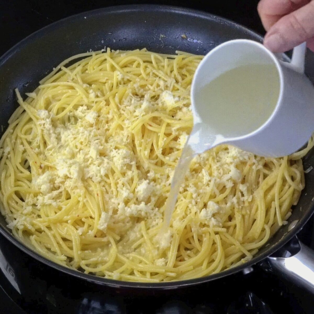 Pouring reserved pasta water into the pan with lemon butter pasta.